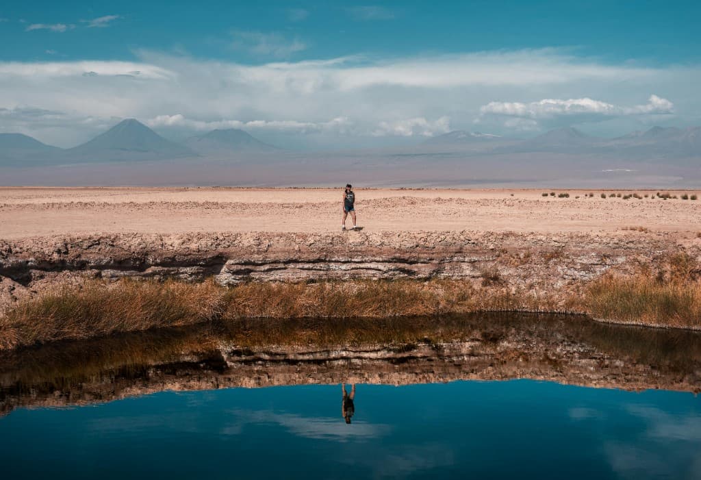 Traveler at an Atacama lagoon with mountain reflections