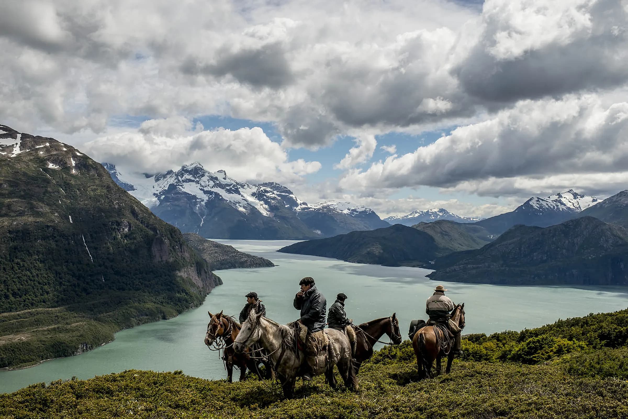 Gauchos on horseback above a lake with the Patagonian mountains behind, near Puerto Natales